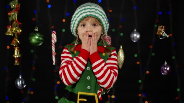 Niña en traje de ayudante de Navidad elfo Santa Claus. Niño haciendo el gesto del ganador, manos wawing - Imágenes, Vídeo