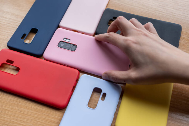 A high angle shot of a hand picking up a phone with colorful phone cases on a wooden table - Fotoğraf, Görsel