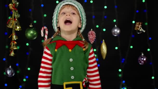 Εφηβικό κοριτσάκι στο Χριστουγεννιάτικο ξωτικό κοστούμι βοηθού του Αϊ Βασίλη που δείχνει τους αντίχειρες στο μαύρο φόντο - Πλάνα, βίντεο