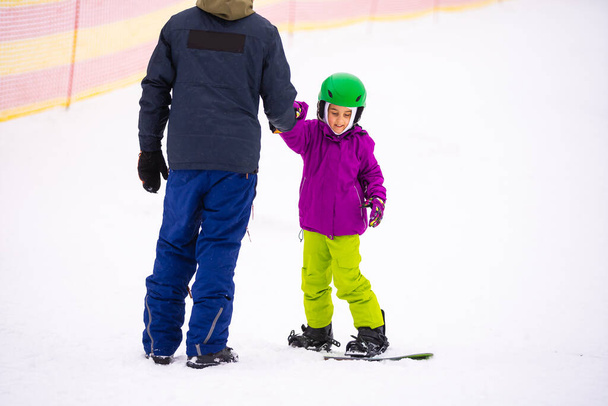 Instruktoren bringen einem Kind auf einem Schneehang das Snowboard bei - Foto, Bild