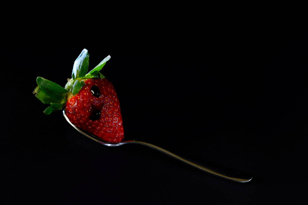 A spoon with a ripe strawberry and a drop of glaze on the surface on the black background with copy space - Fotografie, Obrázek