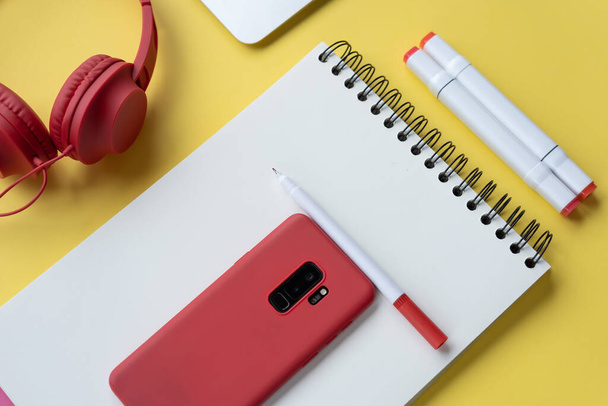 A high angle shot of a journal, marker pens, headphones, and a smartphone on a yellow background - Foto, Bild
