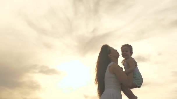 幸せな母親と小さな健康的な子供たちは、太陽の光の中で自然公園で抱き合っています。ママは愛する健康な娘を腕の中で空に投げ出す。休暇中の家族。日没時のお母さんと赤ちゃん. - 映像、動画
