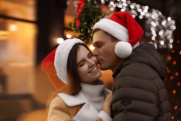 Boldog férfi csókolja a barátnőjét a fagyöngy csokor alatt a szabadban. - Fotó, kép