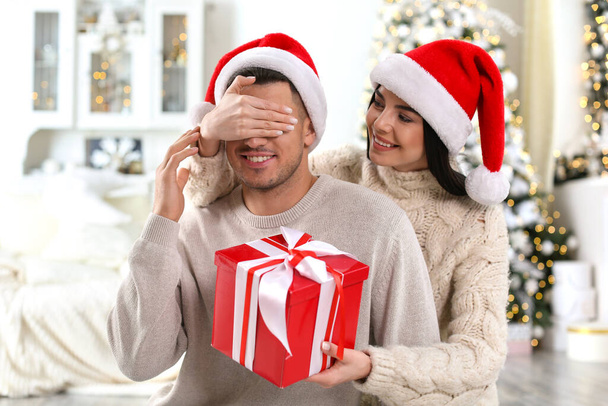 Young woman presenting Christmas gift to her boyfriend at home - Fotografie, Obrázek