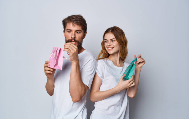 мужчина и женщина с подарочными пакетами стоят спиной друг к другу на сером фоне - Фото, изображение