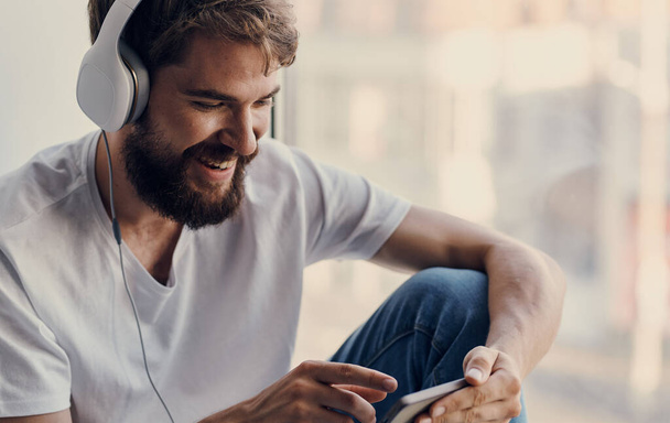 veselý muž ve sluchátkách poslouchá hudbu na parapetu - Fotografie, Obrázek