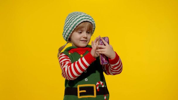 Kid child girl in Christmas elf Santa Claus helper costume making a video call on mobile phone - Foto, Imagem