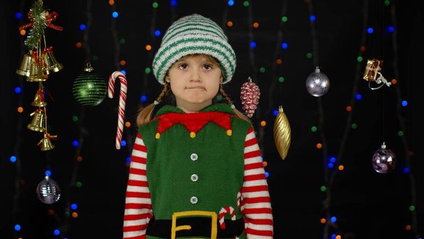 Shy shamed child girl in Christmas elf Santa helper costume posing looking camera making funny faces - Photo, Image