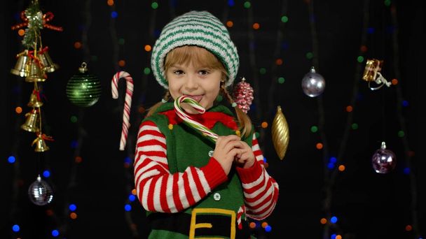 Niña en Navidad elfo Santa Claus ayudante traje lamiendo caramelo bastón piruleta caramelo dulces - Foto, imagen