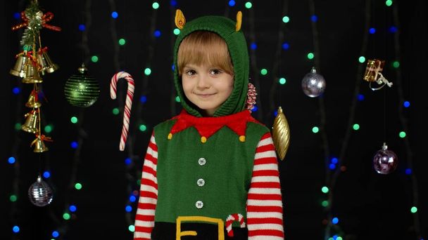 Shy shamed child girl in Christmas elf Santa helper costume posing looking camera and smiling - Photo, Image
