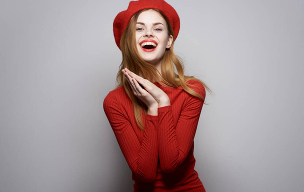 Όμορφη γυναίκα σε κόκκινο φόρεμα καλλυντικά κομψό στυλ συναισθήματα κόκκινο καπέλο γκρι φόντο - Φωτογραφία, εικόνα