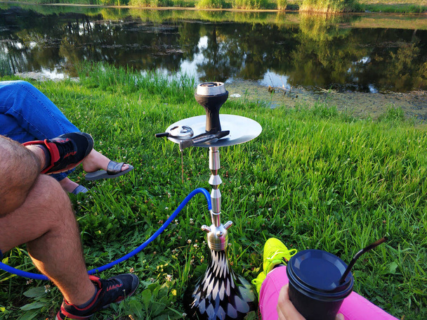 A company of friends smokes a hookah in a green park by the river. Fun with friends. - Fotografie, Obrázek