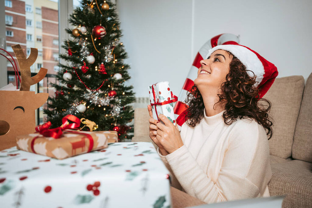 Kaunis brunette nainen hauskaa valmistellessaan joululahjoja olohuoneessa. Hänellä on lahja käsissään ja hän on innoissaan. Joululahjojen valmistelu käsite - Valokuva, kuva