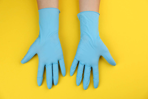 Person in medical gloves on yellow background, top view - Foto, afbeelding