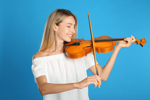 Beautiful woman playing violin on blue background - Foto, afbeelding