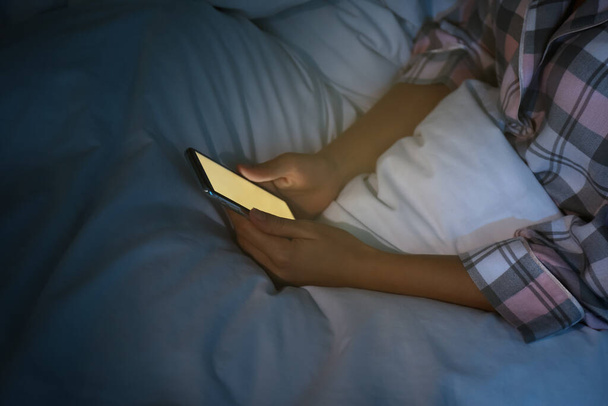 Woman using smartphone in bed at night, closeup. Nomophobia and sleeping disorder problem - Zdjęcie, obraz