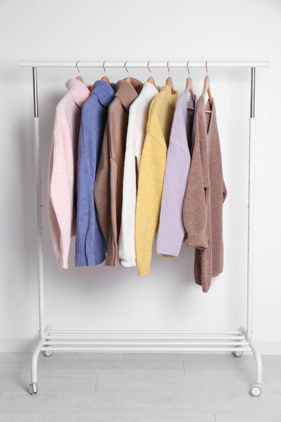 Warm sweaters hanging on rack near white wall - Foto, imagen