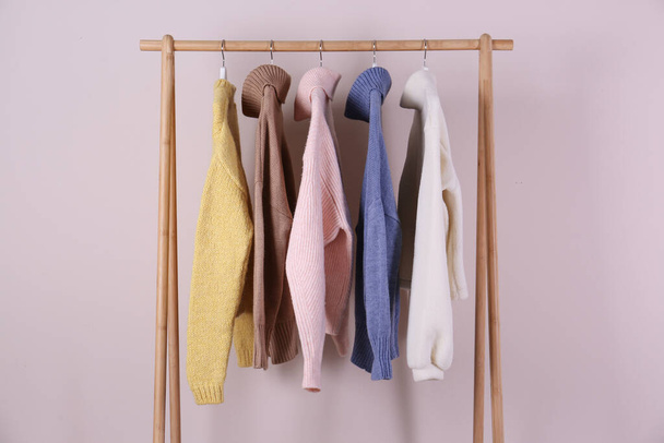 Warm sweaters hanging on wooden rack against pink background - Foto, immagini