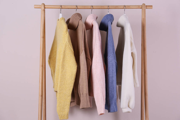 Warm sweaters hanging on wooden rack against pink background - Foto, Imagem