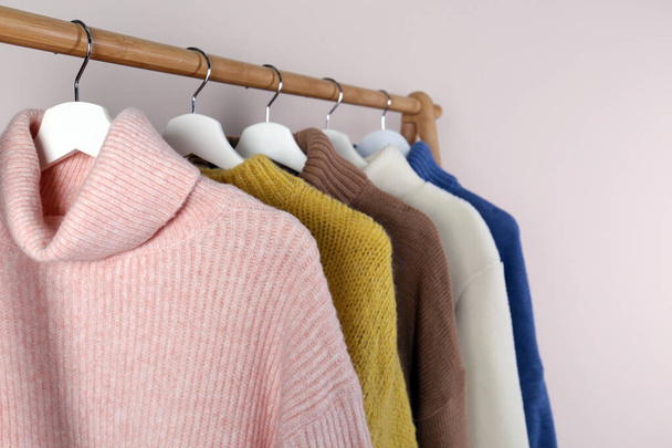 Warm sweaters hanging on wooden rack against light background, closeup - Photo, image