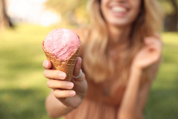 Happy young woman with delicious ice cream in waffle cone outdoors, focus on hand - 写真・画像
