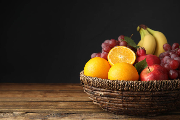 Wicker basket with different fruits on wooden table. Space for text - Φωτογραφία, εικόνα