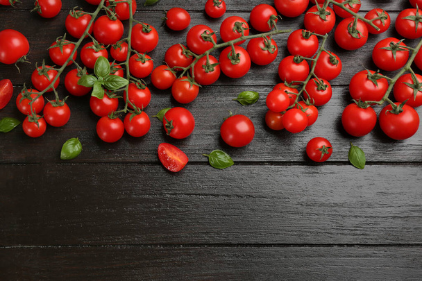 Fresh cherry tomatoes and basil leaves on black wooden table, flat lay. Space for text - Foto, Bild