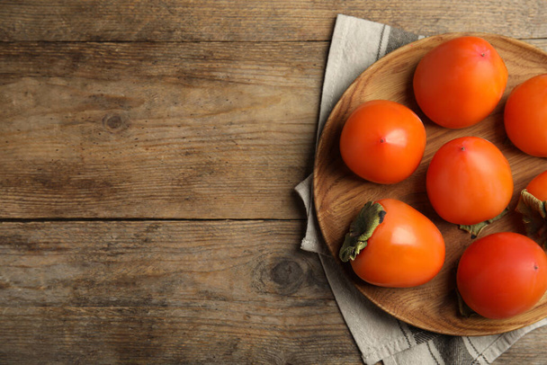 Tasty ripe persimmons on wooden table, flat lay. Space for text - Photo, Image