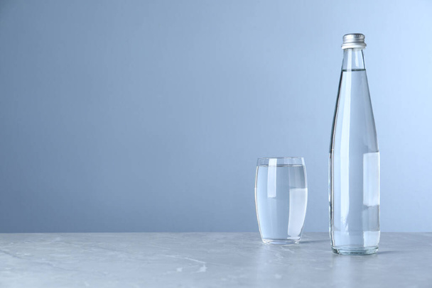 Glass and bottle with water on table against light blue background, space for text - Fotografie, Obrázek
