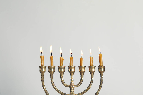 Goldene Menorah mit brennenden Kerzen auf hellgrauem Hintergrund, Platz für Text - Foto, Bild