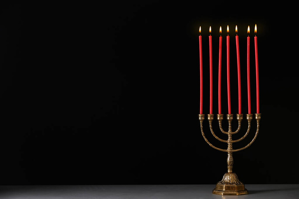 Golden menorah with burning candles on table against black background, space for text - Foto, Imagem