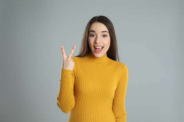 Woman in yellow turtleneck sweater showing number two with her hand on grey background - Photo, Image
