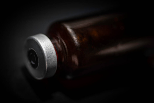 Makro ujęcie z wybiórczym ukierunkowaniem na butelkę zawierającą szczepionkę koloru bursztynowego umieszczoną na czarnym tle. - Zdjęcie, obraz