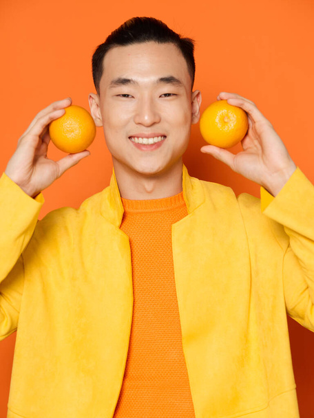 Elinde portakal olan neşeli bir adam izole bir arka planı ve sarı bir ceketi var. - Fotoğraf, Görsel