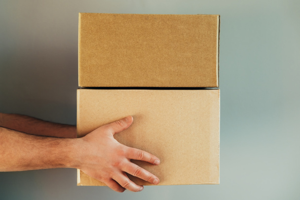 The hands of delivery service man delivers carton boxes on the grey background. Delivery service, online shopping and logistic concept. - Φωτογραφία, εικόνα