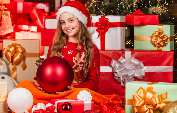 Merry christmas. Happy childhood concept. Kid santa hat christmas gift boxes. Santa brought me gifts. Gifts shop. Magical and cozy. Happiness and joy. Child happy girl find gifts near christmas tree - 写真・画像