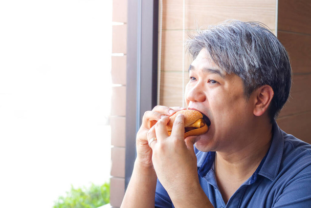Los hombres gordos son asiáticos que comen hamburguesas en un restaurante de comida. - Foto, Imagen