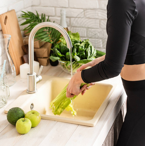 Die Zubereitung gesunder Lebensmittel. Junge lächelnde Frau in Sportkleidung wäscht Sellerie in der Küche - Foto, Bild