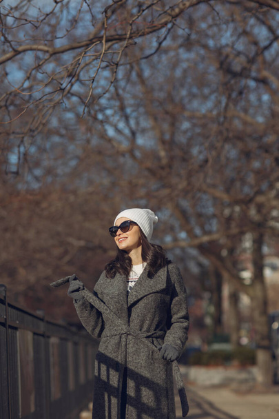 Elegant meisje wandelen in een winterstad. Vrouw in een witte gebreide trui. Mooie dame met donker haar. - Foto, afbeelding