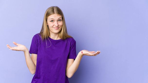 Young blonde woman isolated on purple background doubting and shrugging shoulders in questioning gesture. - Photo, Image