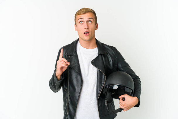 Joven hombre caucásico sosteniendo un casco de moto aislado sobre fondo blanco apuntando al revés con la boca abierta. - Foto, imagen