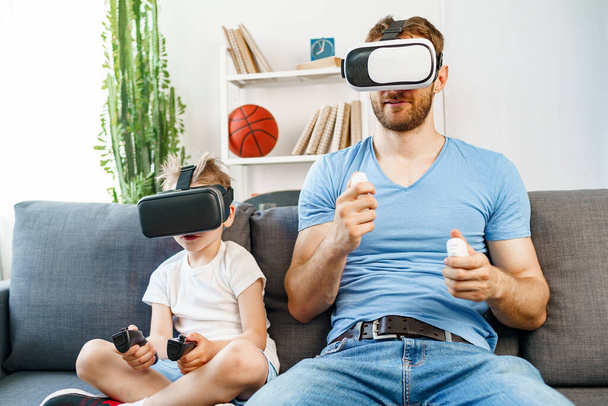 Vater und Sohn sitzen auf Sofa und spielen mit VR-Brille - Foto, Bild