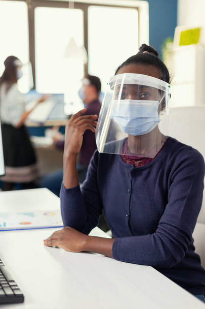 Επιχειρηματίας κάθεται στο χώρο εργασίας της φορώντας μάσκα προσώπου - Φωτογραφία, εικόνα
