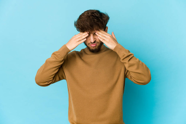 Young arab man on blue background having a head ache, touching front of the face. - 写真・画像