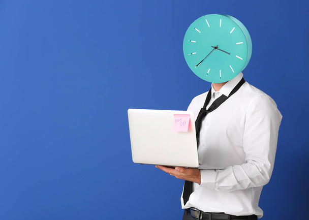 Young businessman with clock instead of head and laptop on color background. Time management concept - Fotografie, Obrázek