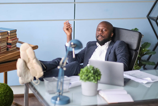 Ontspannen werknemer klaar met het werk voltooid taak nemen pauze na harde werkdag het hoofd op de hand. Bedachtzame Afro-Amerikaanse zakenman kijkt uit het raam zittend aan het bureau. - Foto, afbeelding