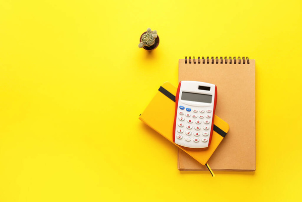 Digitale rekenmachine, notebooks en cactus op kleur achtergrond - Foto, afbeelding