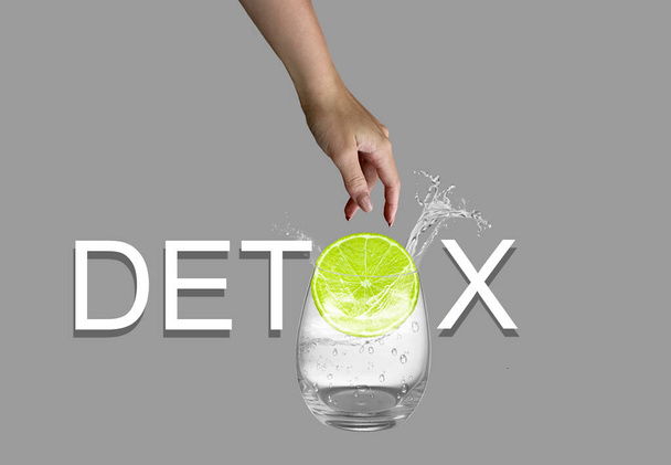 White detox text isolated on gray background. Female hand throwing slice of lemon to glass of water. - Photo, Image