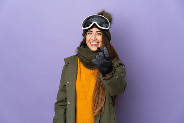 Скромна біла дівчина зі сноубордистськими окулярами ізольована на фіолетовому фоні, роблячи прийдешній жест
 - Фото, зображення